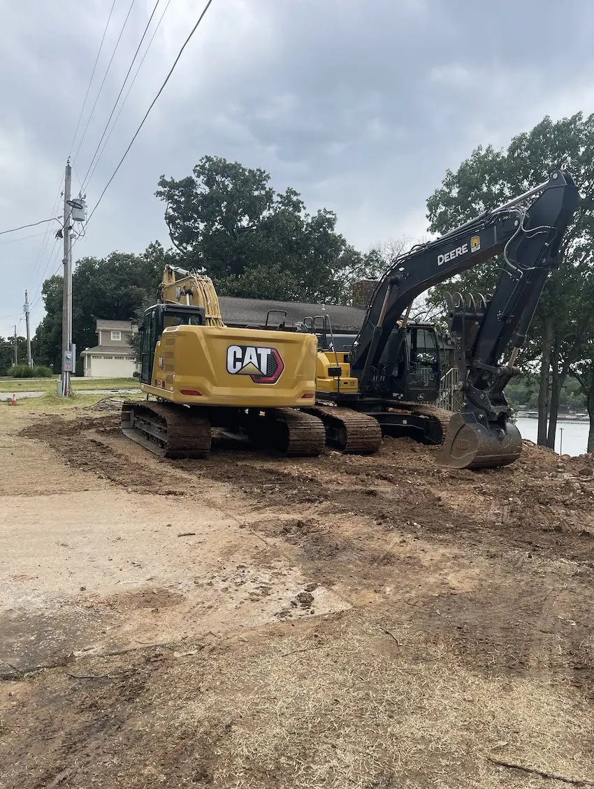 Two tracked excavators on cleared, graded ground beside a house