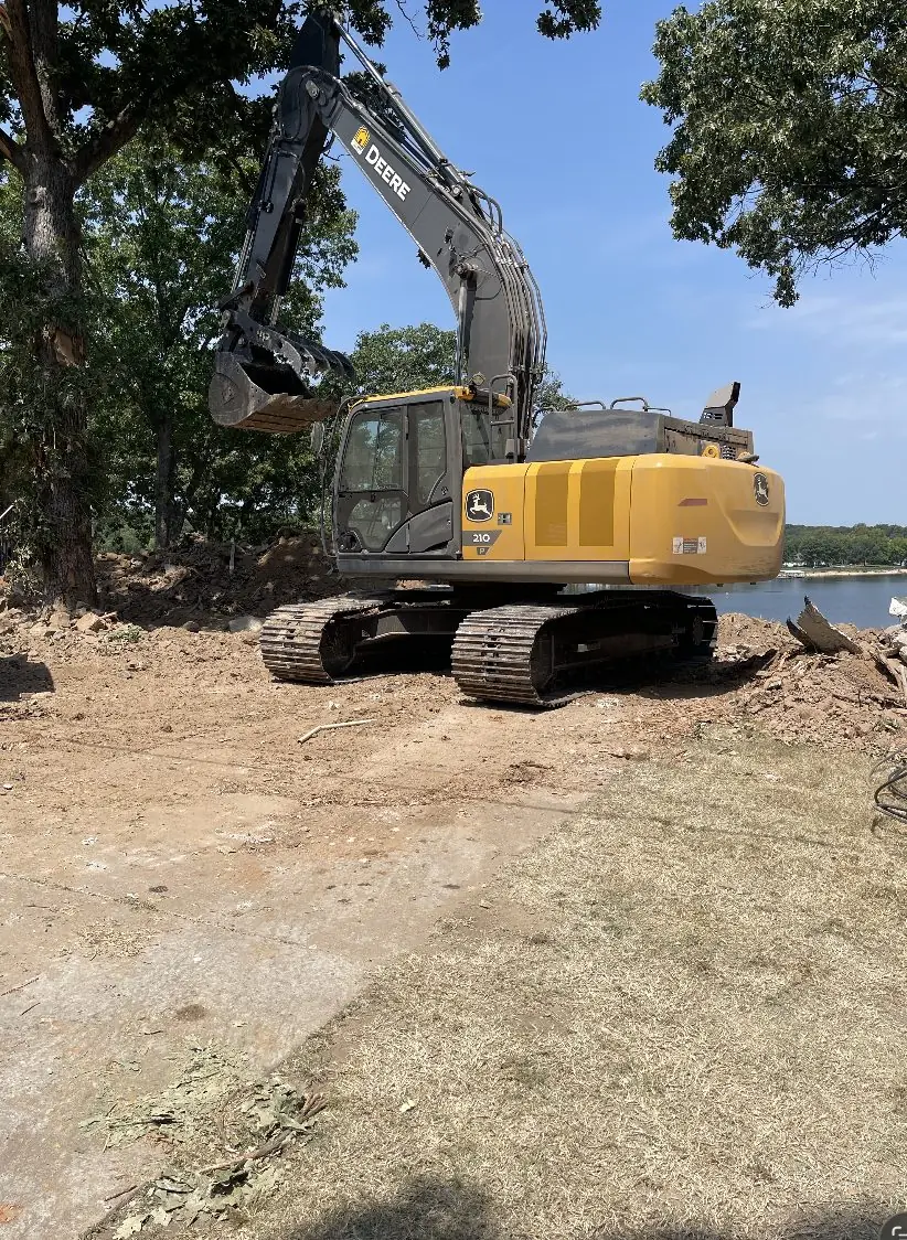 Excavator working at the edge of a wooded lakeside lot