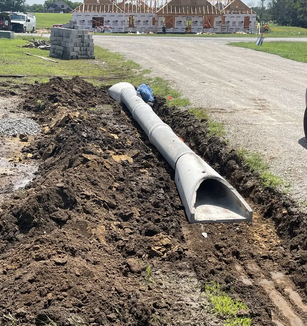 Trench dug beside a gravel road with a large concrete pipe ready to go in