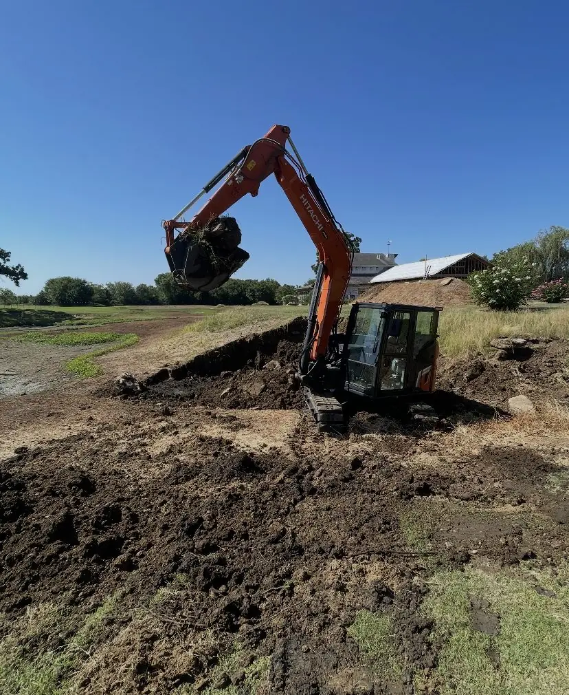 Orange excavator digging out a pond bank beside a field