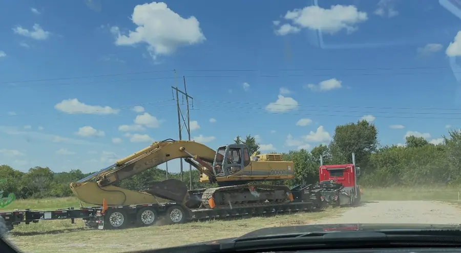 Excavator loaded on a lowboy trailer behind a red truck